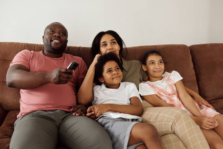 A family of four enjoying quality time together on the sofa, watching TV with smiling faces.