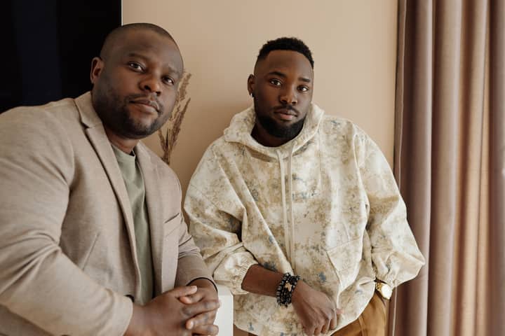 Two stylish African American men posing confidently indoors, showcasing fashion and expression.