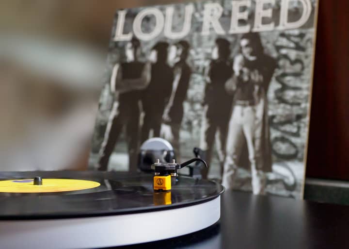 Close-up of a turntable spinning a vinyl with Lou Reed album in the background.