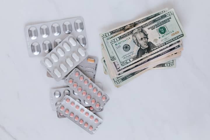 From above of silver blister full of drug near big pile of dollar to spend on medication