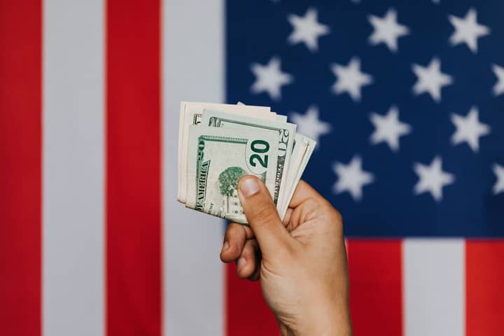 Unrecognizable male demonstrating dollars before official flag of USA on background