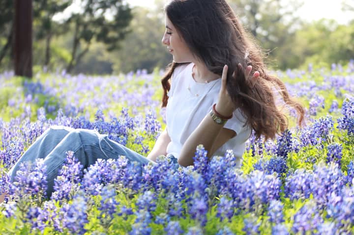 A serene scene of a young woman sitting amidst a blooming field of bluebonnets during a sunny day in Austin, Texas.