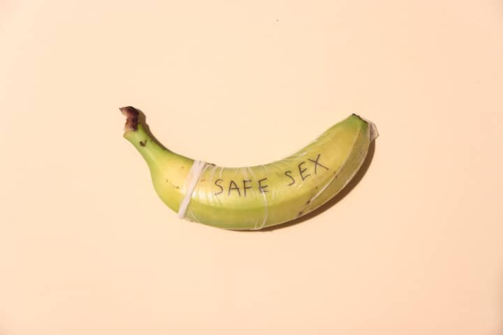 A banana wrapped in a condom for safe sex awareness on a pastel background.