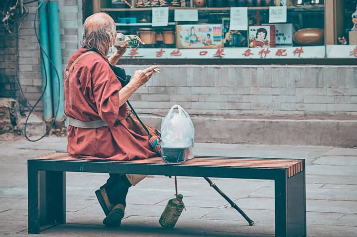 Senior man in traditional attire drinks on Beijing street, exuding a sense of tranquility.