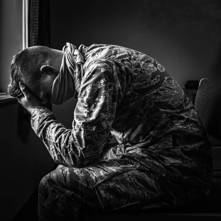 Black and white of upset soldier man in uniform sitting and leaning forehead on hands in sufferings