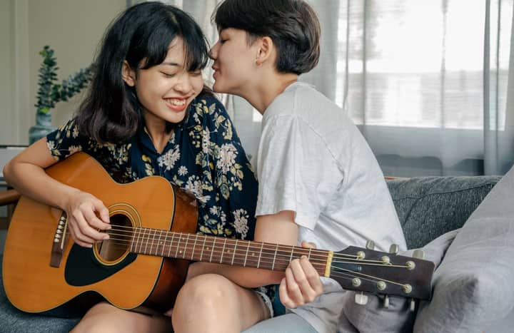 A joyful couple playing guitar and sharing affectionate moments indoors.