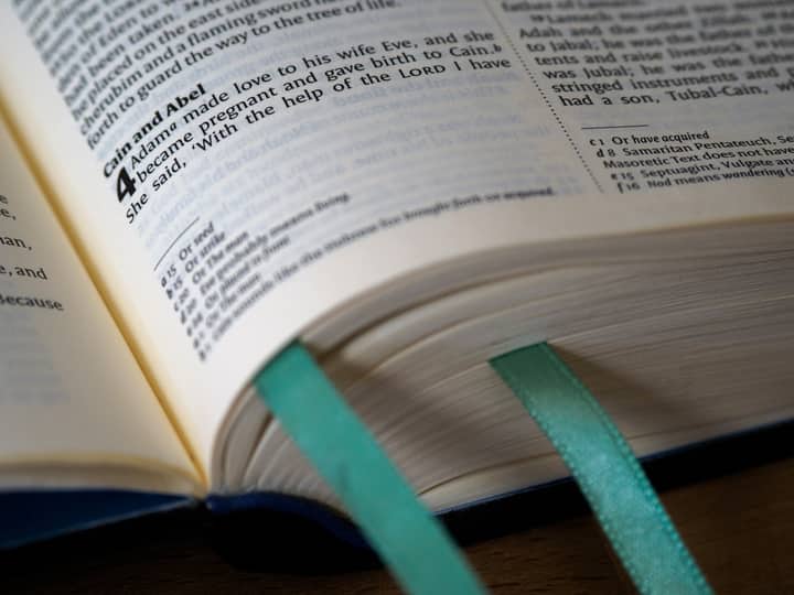 Open Bible showing Genesis, Cain and Abel story, with teal bookmarks.