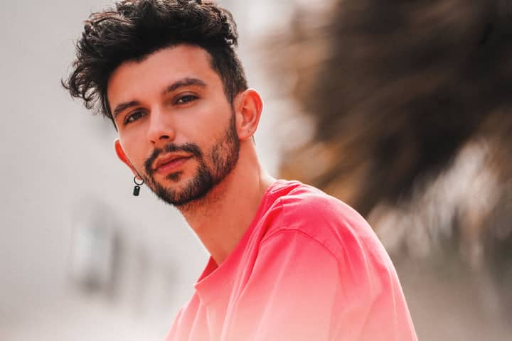 Portrait of a stylish young man outdoors in casual attire, featuring a beard and fashionable look.