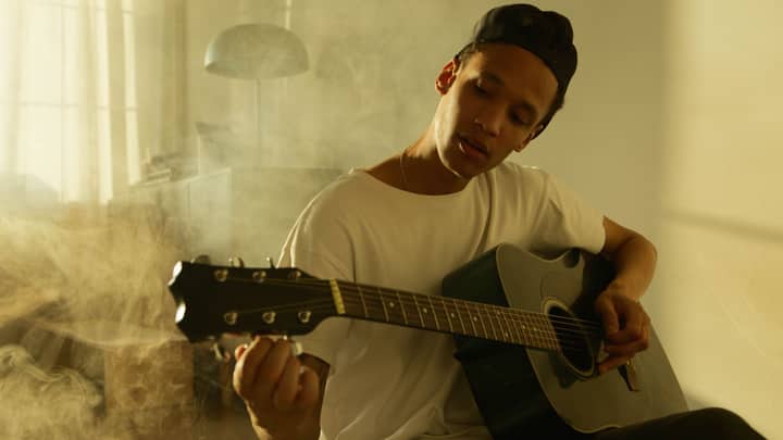 A young man enjoys playing an acoustic guitar in a sunlit room, expressing passion for music.