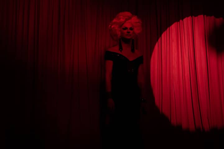 A captivating drag queen in a glamorous black dress on stage with red lighting, capturing nightlife performance.