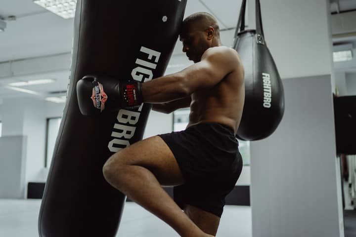 A focused shirtless man trains with a punching bag in a gym, showcasing strength and determination.