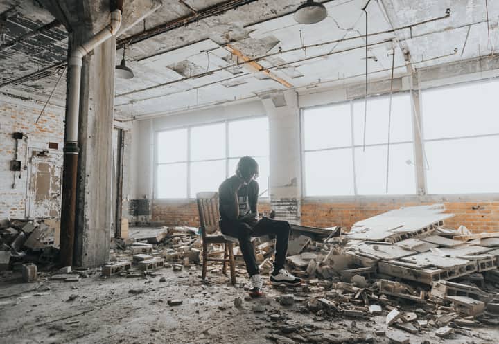 A person sits in a desolate, crumbling space filled with debris, conveying a powerful sense of abandonment.
