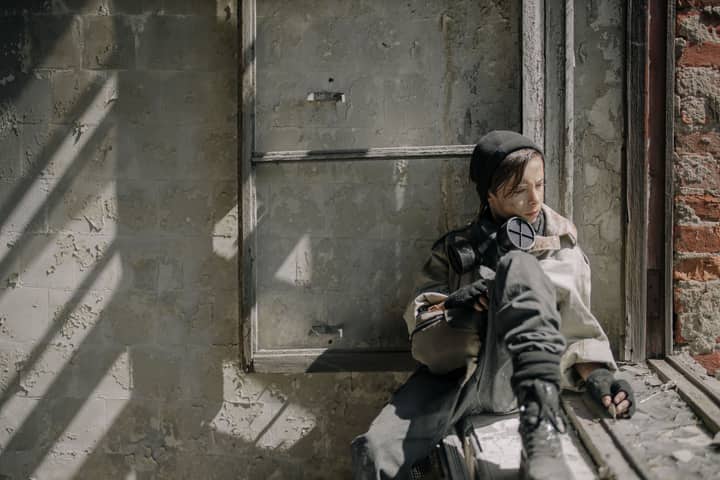 A young person sits in a dilapidated building, symbolizing isolation in a post-apocalypse world.