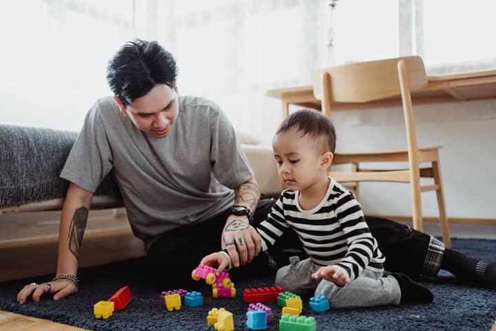A father and son playing with colorful building blocks in a cozy indoor setting.
