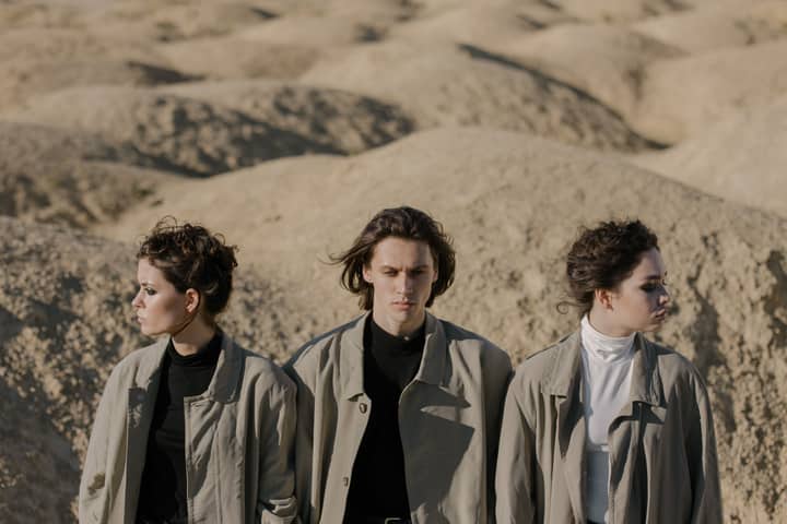 Fashionable group wearing overcoats stands in a desert setting.