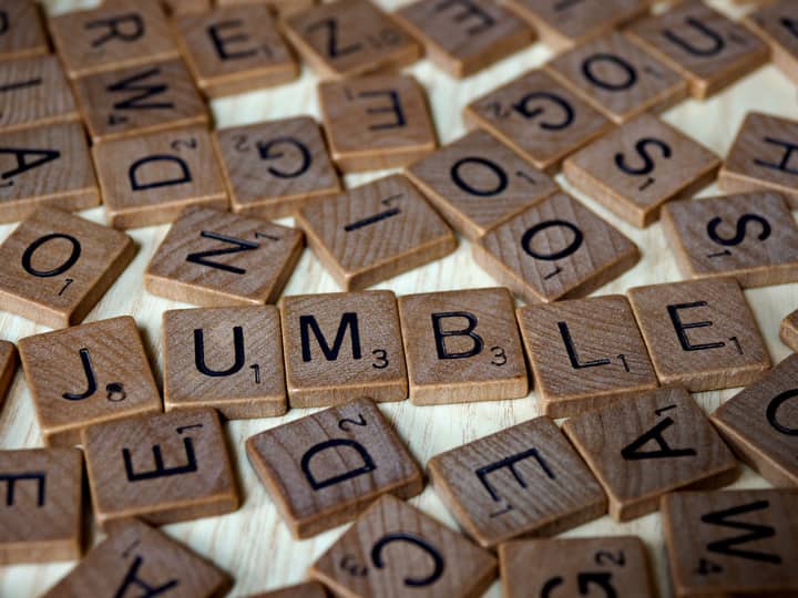 Close-up of scattered Scrabble tiles forming the word 'jumble' on a wooden surface.
