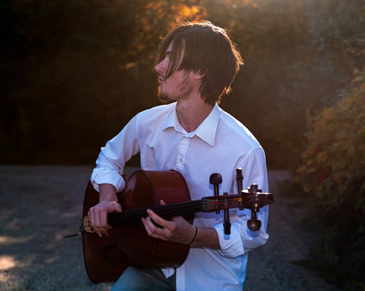 A young man plays the cello outdoors during sunset, creating a serene musical atmosphere.