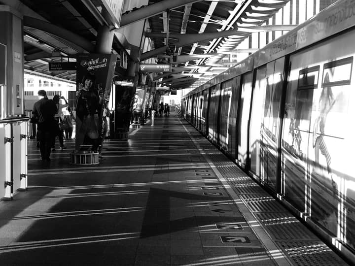 Black and white image capturing commuters at a railway platform in Khwaeng Samsen Nai, Bangkok, Thailand.