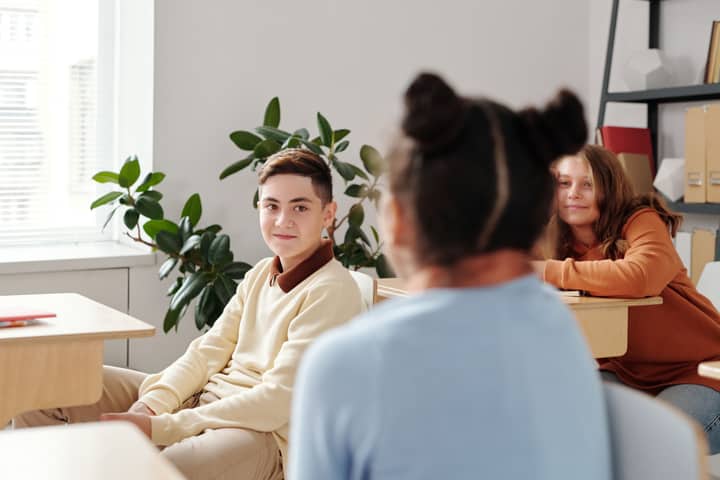 Diverse group of teenagers interacting in a bright classroom setting with natural lighting.