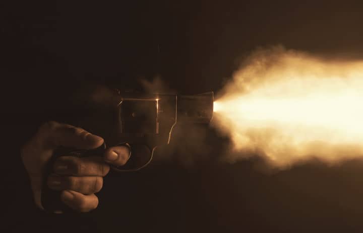 Close-up of a handgun firing with a bright flash in a dark setting, creating a dramatic effect.