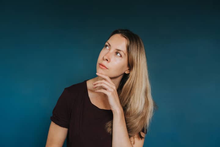 Young thoughtful female in casual clothes touching chin while standing in studio and looking up
