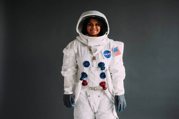 Portrait of a woman in a NASA astronaut costume, smiling against a neutral background.