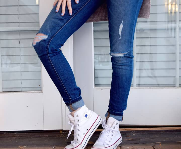 A stylish display of ripped jeans paired with classic white high-top sneakers.
