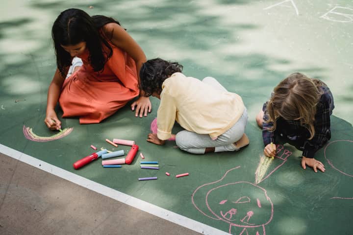 Kids creatively using chalk on outdoor pavement, enjoying a sunny day.
