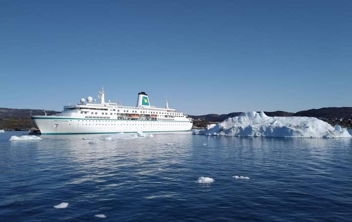 A cruise ship sails near icebergs in Ilulissat, Greenland, on a clear sunny day.