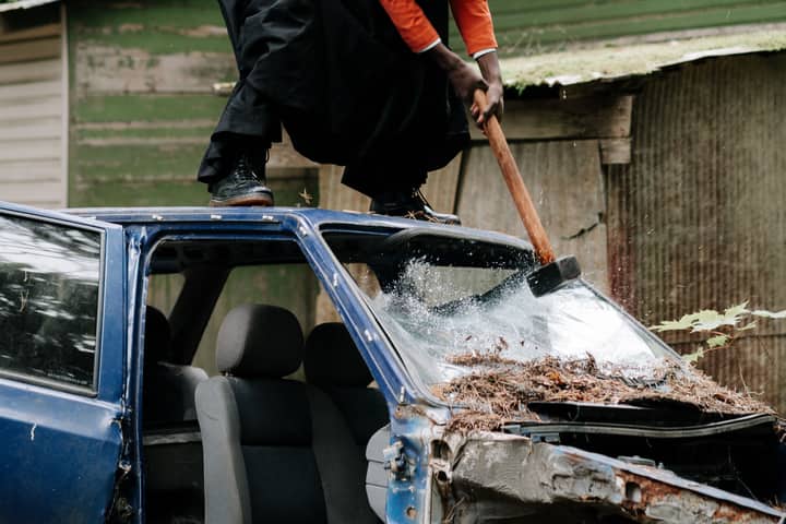 A man aggressively smashes a car windshield with a sledgehammer in an outdoor setting.