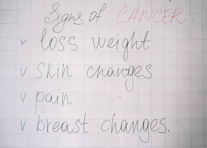 List of cancer symptoms handwritten on a whiteboard including weight loss and skin changes.