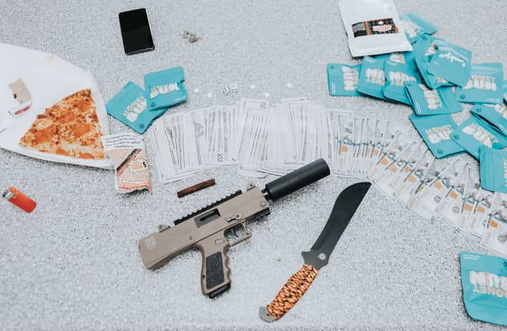 Close-up view of cash, a firearm, and a knife on a table with a slice of pizza.