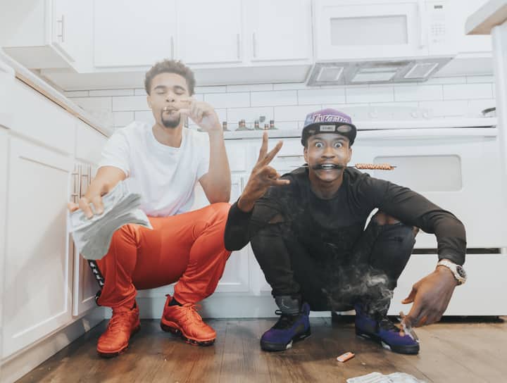 Two young men pose indoors in a relaxed setting, capturing a moment of urban lifestyle.