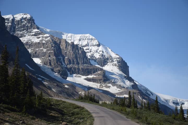 Explore the breathtaking snow-covered mountains in Cody, Wyoming, with clear blue skies and a winding road.