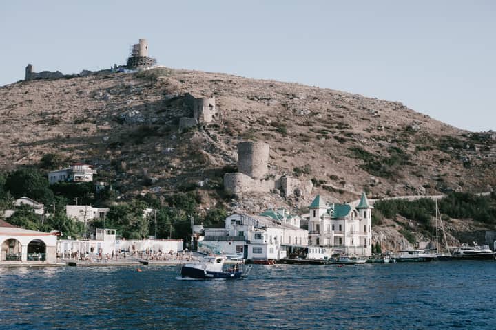 Scenic view of a historic coastal town with boats anchored at the harbor against hilly ruins.
