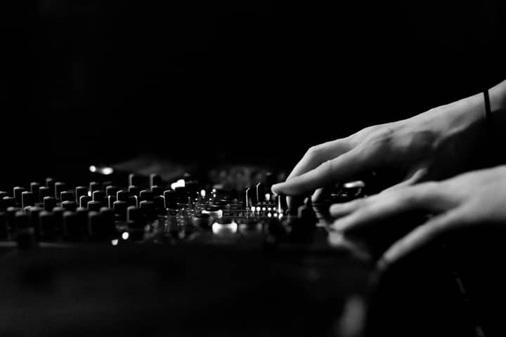 Artistic black and white image of hands adjusting a DJ console in a club.