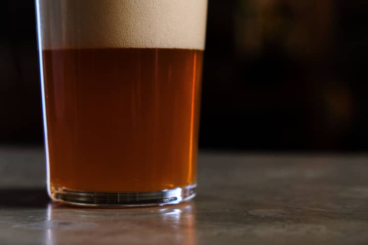 A detailed shot of a glass of amber craft beer topped with foam, set against a dark background.