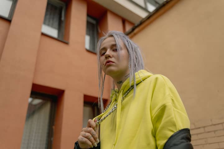 Trendy woman wearing neon hoodie and chain necklace in urban outdoors setting, embodying modern fashion.
