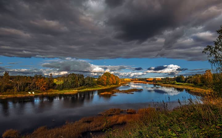 Stunning autumn view of Pärnu River with dark clouds and vibrant foliage in Estonia.