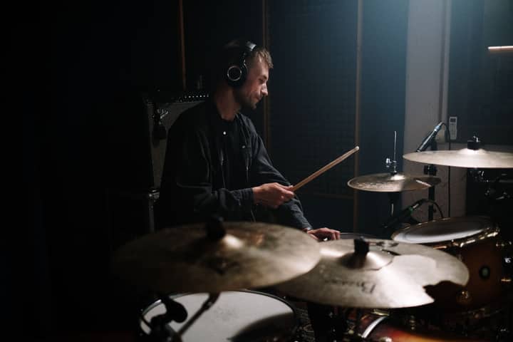 A man playing drums with headphones in a recording studio, perfect for music themes.