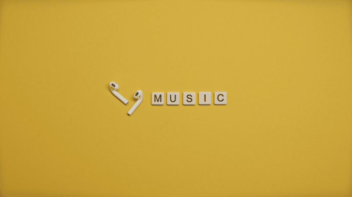 Minimalist image of AirPods and music-themed letter tiles on a vibrant yellow background.