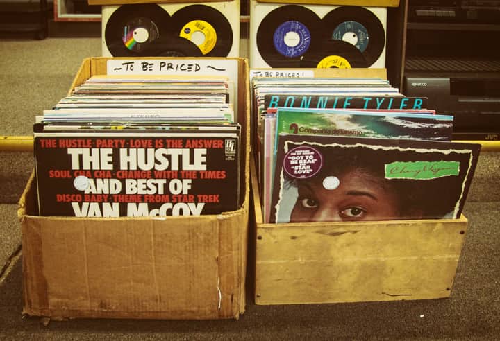 Two boxes of assorted vinyl records in a retro shop setting for sale.