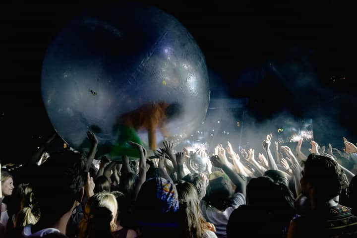 Anonymous people with raised arms holding transparent walking ball with person during entertainment at night