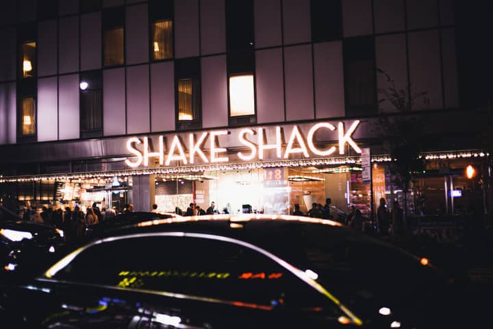 Vibrant scene outside a busy Shake Shack restaurant at night with glowing signage.