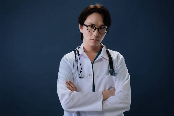 Portrait of a doctor with eyeglasses and stethoscope against a blue background in professional attire.