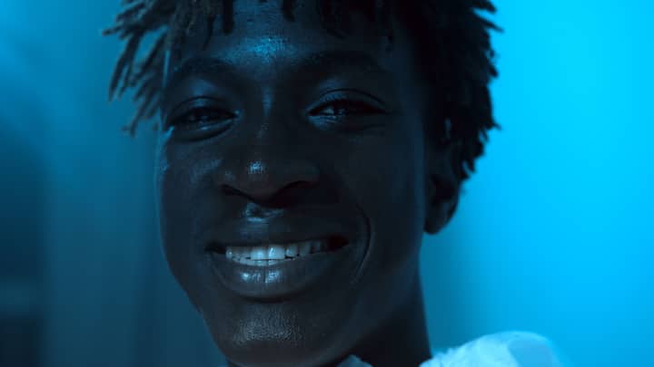 Close-up portrait of a smiling black man with a vibrant blue background highlighting his joyful expression.