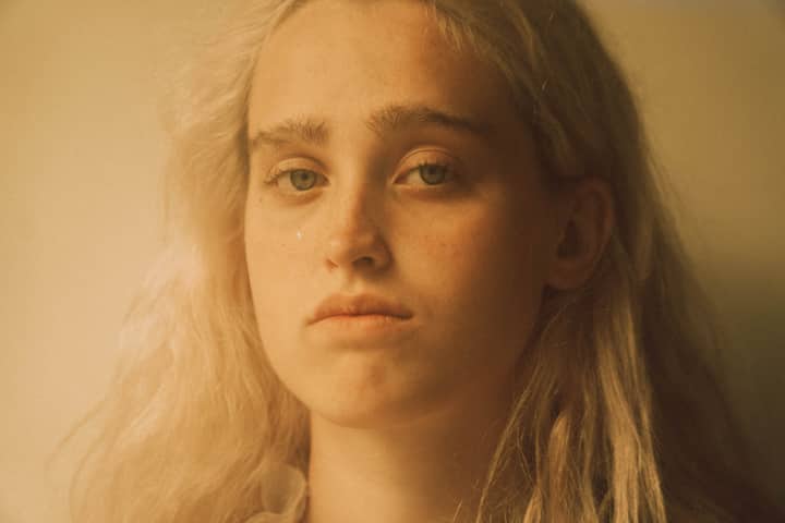 Crop young sensitive female with blond hair and teardrop on cheek looking at camera