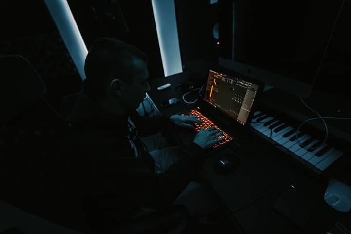 Music producer focused on composing tracks in a dimly lit studio with laptop and keyboard.