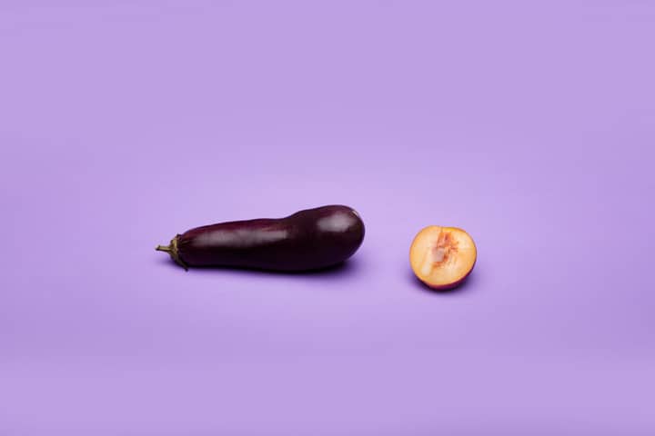 Conceptual art featuring an eggplant and a peach on a purple background symbolizing sexuality.