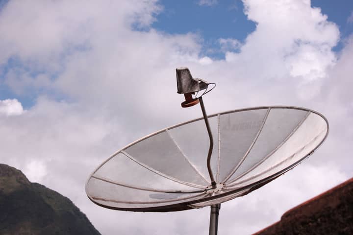Silver satellite dish pointing skyward under a bright blue sky with scattered clouds.